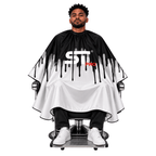 Seated client wearing a black-and-white drip-design barber cape