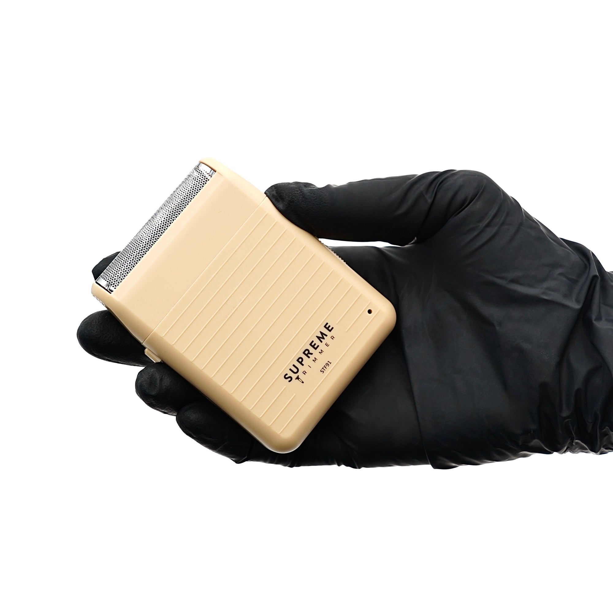 Beige electric razor held by a gloved hand on a white background