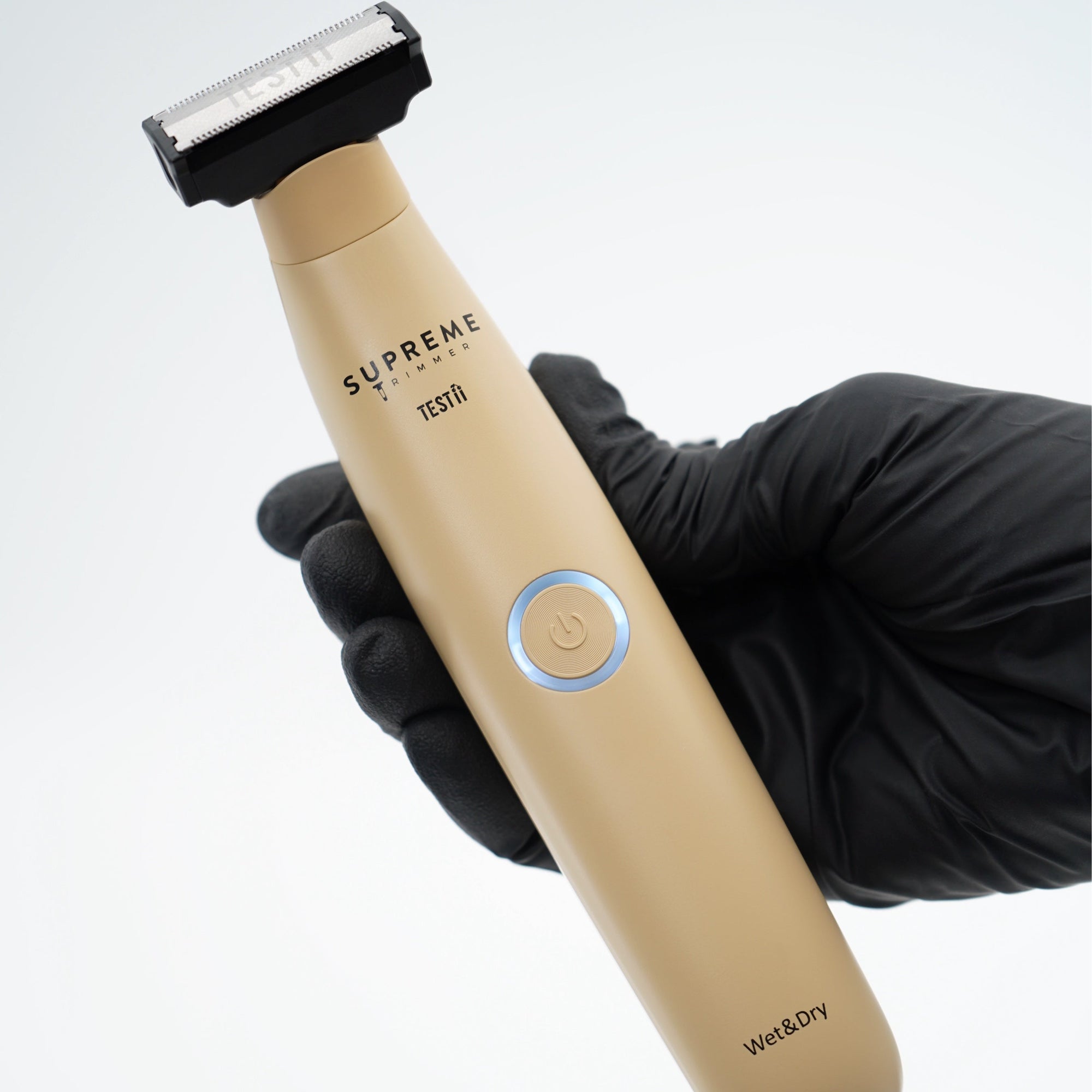 Beige electric shaver held by a gloved hand on a light gray background